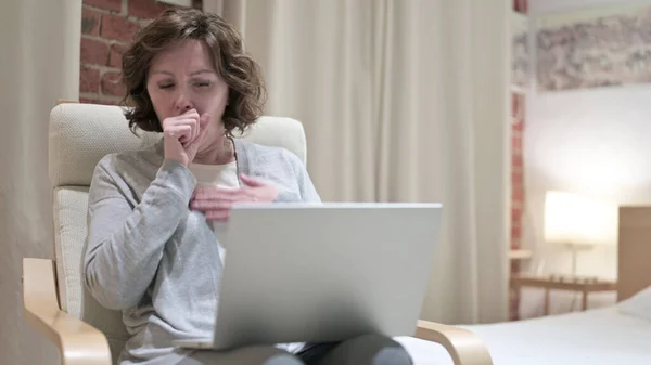 Sick Old Woman Coughing while Using Laptop on Chair