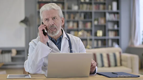 Oudere arts in gesprek over Smart Phone in de kliniek — Stockfoto