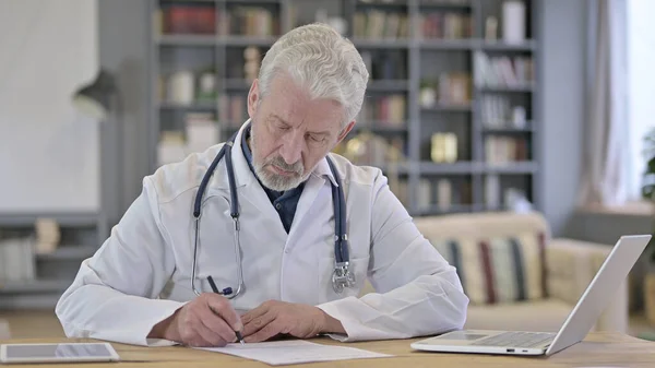 Senior Old Doctor doing Paperwork in Clinic