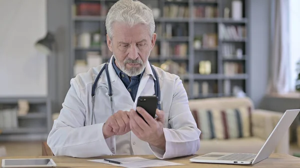 Focused Senior Old Doctor using Smartphone in Clinic