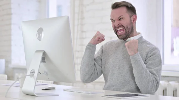Excited Young Man Celebrating Success on Desktop