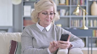 Kanepede akıllı telefon kullanan yaşlı kadın.