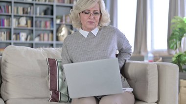 Dizüstü bilgisayarda çalışan ve sırt ağrısı çeken yorgun yaşlı kadın.