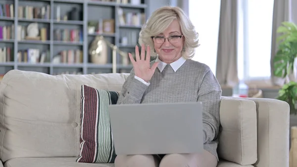 Oude vrouw zit op de bank en doet videochat op laptop — Stockfoto
