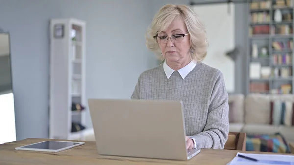 Vieille femme sérieuse utilisant un ordinateur portable dans le bureau moderne — Photo