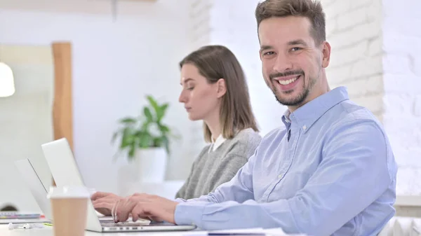 Alegre hombre creativo trabajando en el ordenador portátil y sonriendo a la cámara — Foto de Stock