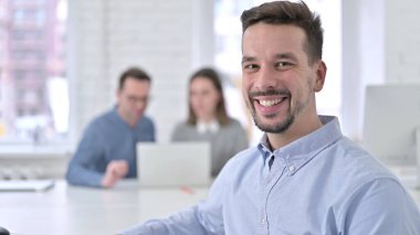 Ofisteki kameraya gülümseyen neşeli genç adam.