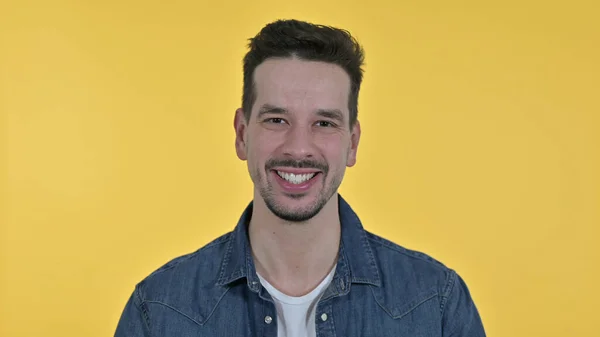 Uśmiechnięty młody człowiek patrzący w kamerę, żółte tło — Zdjęcie stockowe