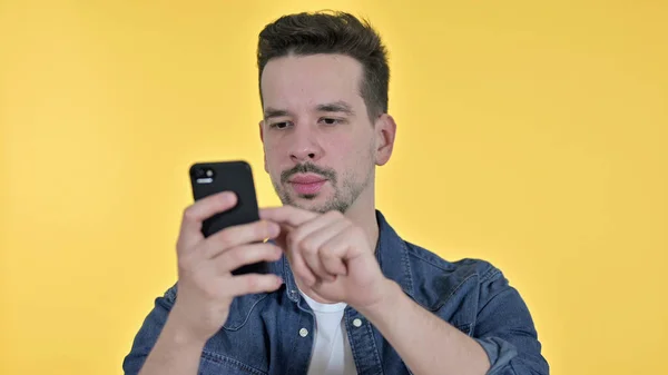 Hombre joven atractivo usando Smartphone, fondo amarillo —  Fotos de Stock