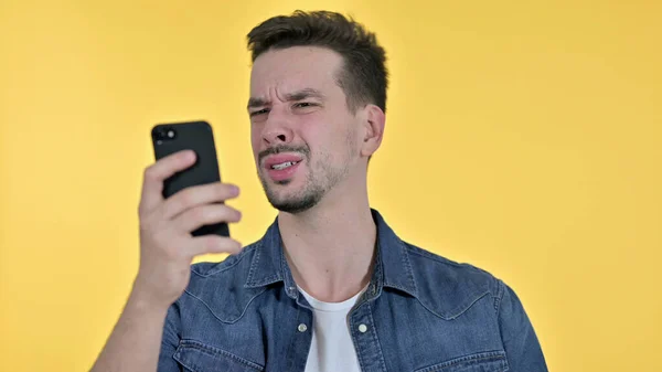 Jeune homme réagissant à la perte sur Smartphone, fond jaune — Photo