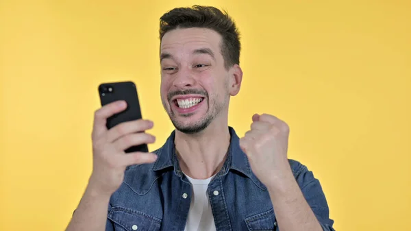 Mladý muž slaví úspěch na Smartphone, žluté pozadí — Stock fotografie