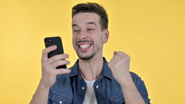 Young Man Celebrating Success on Smartphone, Yellow Background — ストック写真