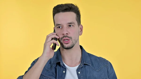 Irritado jovem homem ficando irritado no smartphone, fundo amarelo — Fotografia de Stock
