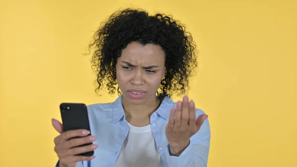 Afrikansk kvinna som reagerar på förlust på smartphone, gul bakgrund — Stockfoto