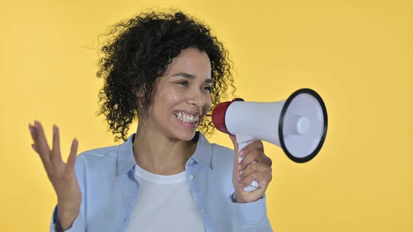 Afrikansk kvinna gör tillkännagivande på högtalare, gul bakgrund — Stockfoto