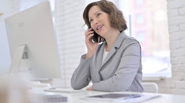 Ofiste akıllı telefondan konuşan yaratıcı yaşlı kadın.