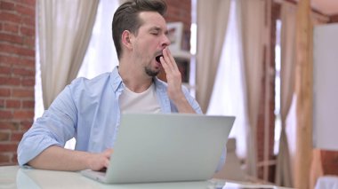 Genç adam Yawing 'e sahip ve laptopta çalışıyor.