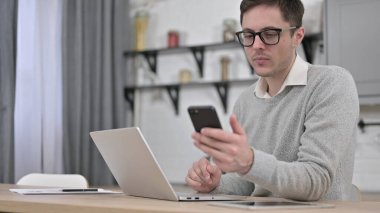 Akıllı telefon ve dizüstü bilgisayar kullanan genç adam