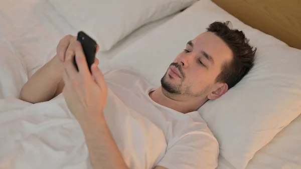 在床上用智能手机的年轻人 — 图库照片