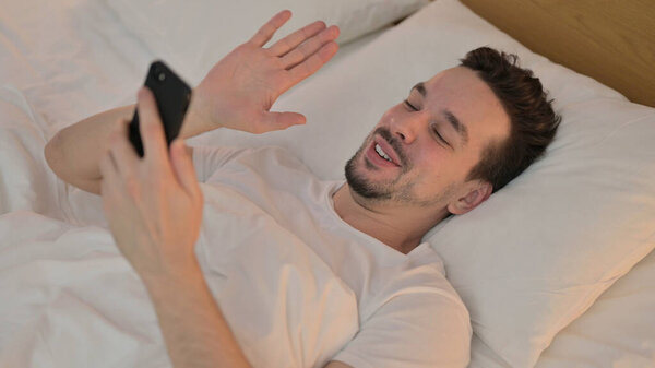 Young Man doing Video Chat on Smartphone in Bed