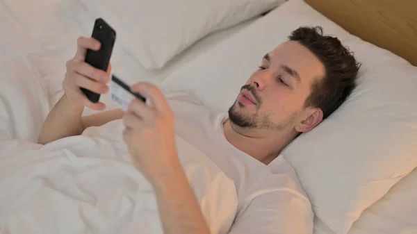 年轻人在床上智能手机上的网上购物 — 图库照片