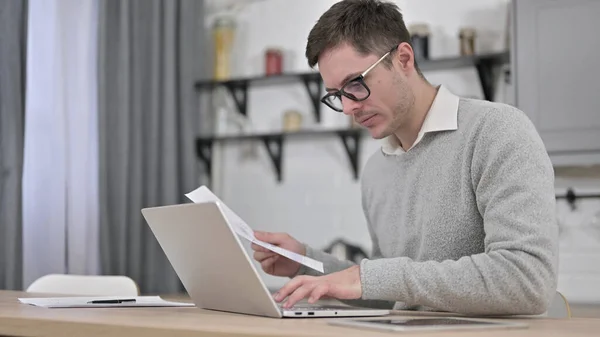 Jonge man met behulp van laptop voor papierwerk — Stockfoto