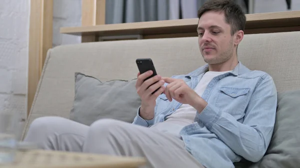 Relaks Młody człowiek za pomocą smartfona w salonie — Zdjęcie stockowe