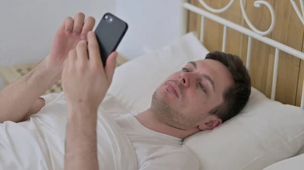 Attractive Young Man using Smartphone in Bed — Stock Photo, Image