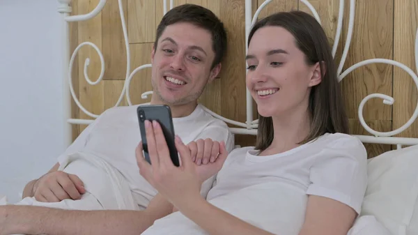 一对年轻夫妇在床的智能手机上做视频聊天 — 图库照片