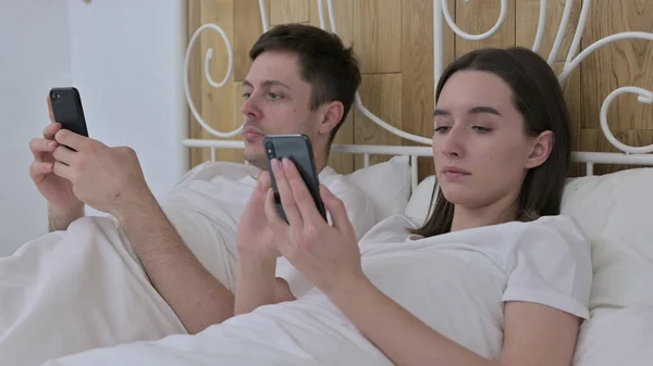 Atrakcyjna młoda para za pomocą smartfona w łóżku — Zdjęcie stockowe
