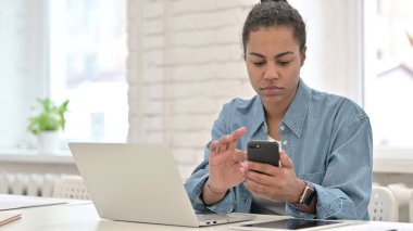 Akıllı telefon ve dizüstü bilgisayar kullanan genç Afrikalı kadın.