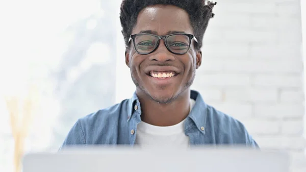 Portrét mladého afrického muže usmívajícího se a pracující na notebooku — Stock fotografie