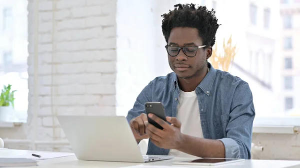 Mladý Afričan používající smartphone v kanceláři — Stock fotografie