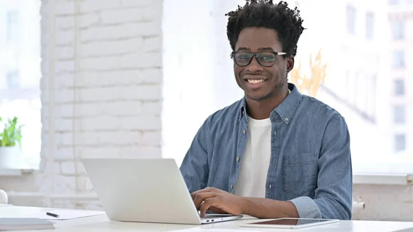 Jonge Afrikaanse man werkt en glimlacht bij de camera — Stockfoto