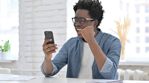Mladý africký muž jásající Vyhrajte na chytrém telefonu — Stock fotografie