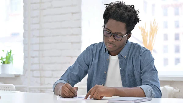 Młody Afrykanin pisze na dokumencie w biurze — Zdjęcie stockowe