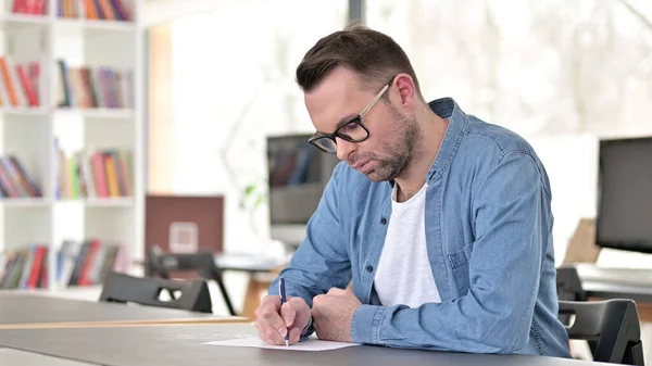 Young Man in Glasses Writing on Paper