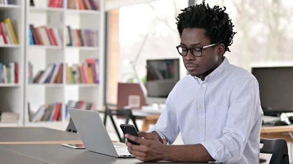 African Man pomocí smartphonu a notebooku — Stock fotografie