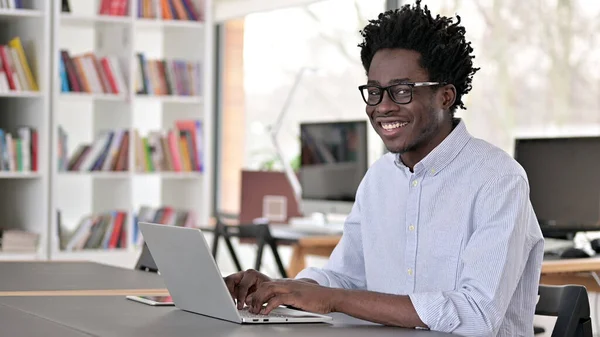 Afrikaanse man glimlachen op de camera tijdens het werken op laptop — Stockfoto