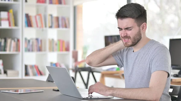 Jovem com dor no pescoço usando laptop no escritório — Fotografia de Stock