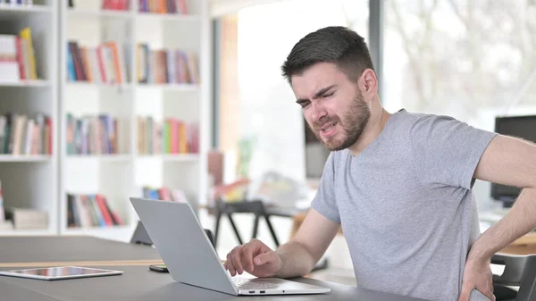 Jongeman met laptop met rugpijn in het kantoor — Stockfoto