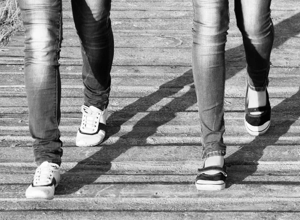 Benen av två flickor i jeans och bekväma skor medan promenader / svart och vit foto — Stockfoto