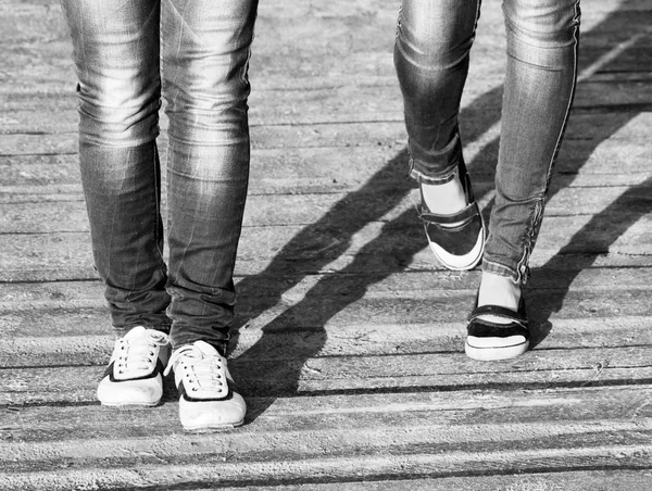 Las piernas de dos niñas en jeans y zapatos cómodos mientras camina / Foto en blanco y negro —  Fotos de Stock