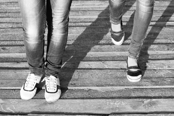 The legs of two girls in jeans and comfortable shoes while walking / Black and white photo — Stock Photo, Image