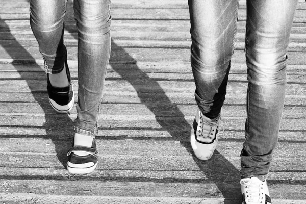 Las piernas de dos niñas en jeans y zapatos cómodos mientras camina / Foto en blanco y negro — Foto de Stock