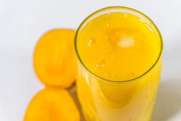 Mango džus lichotníku lesklý bílý stůl. Čerstvé zdravý nápoj. — Stock fotografie