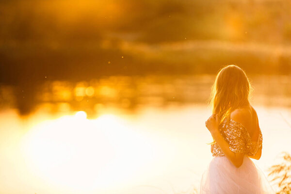 Portrait of a beautiful girl in a dress at sunset near a lake