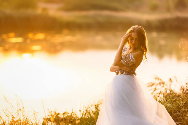 Portrait of a beautiful girl in a dress at sunset near a lake