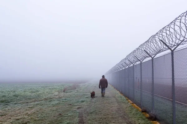 Man en hond wandelen langs het hek in de mist — Stockfoto