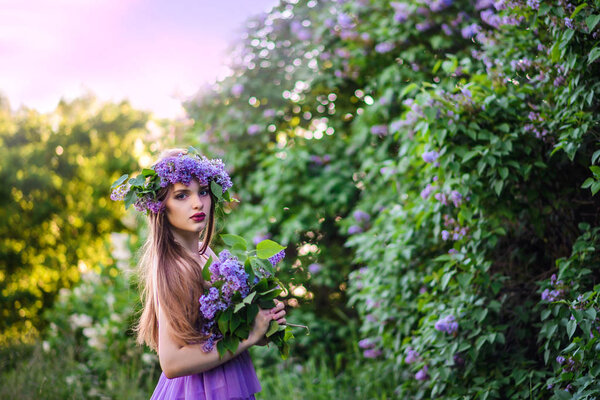 The girl with the wreath on his head in the lilac bushes